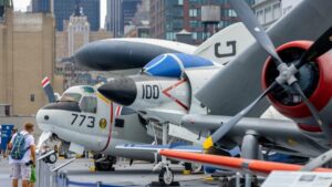 Two WW2 era planes sitting on a deck with a man looking at them